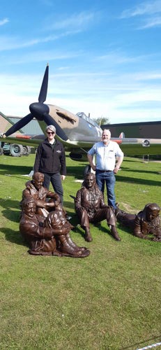 Sarah Nathinel, left, poses in front of a Spitfire alongside a member of staff from the Battle of Britain Museum. A number of bronze statues of WW2 airmen are on the lawn in front of the two people.