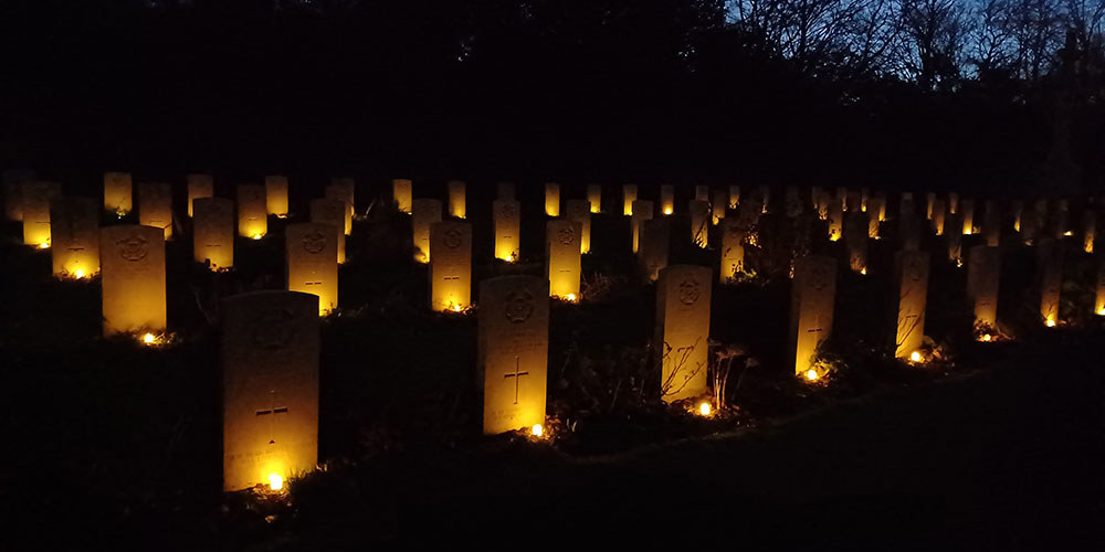 Several rows of CWGC headstones illuminated from each base by a small candle. The night sky is a dark black.