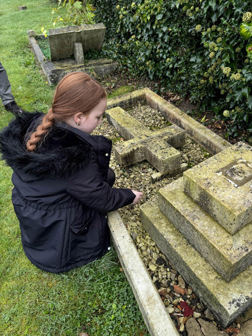 A redheaded primary schoolgirl lays a memorial stone on the grave of a World War soldier.