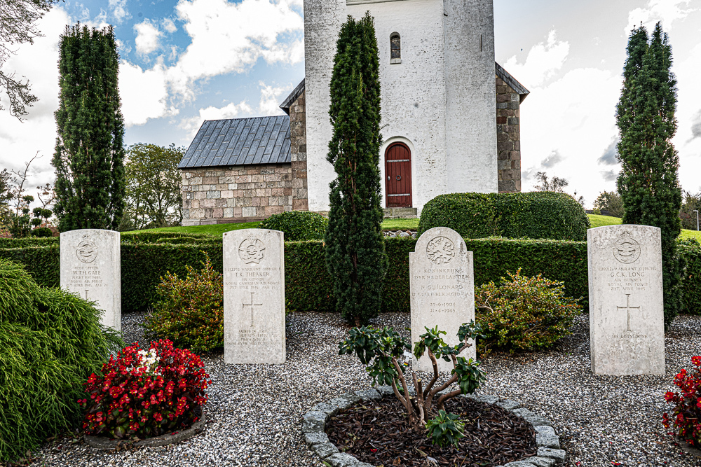 Row of CWGC headstones in a Danish churchyard. A tall white stone church tower with a banded red wooden door is visible in the background.