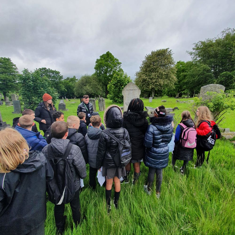 Schoolchildren listen to a volunteer speaker in a CWGC cemetery.