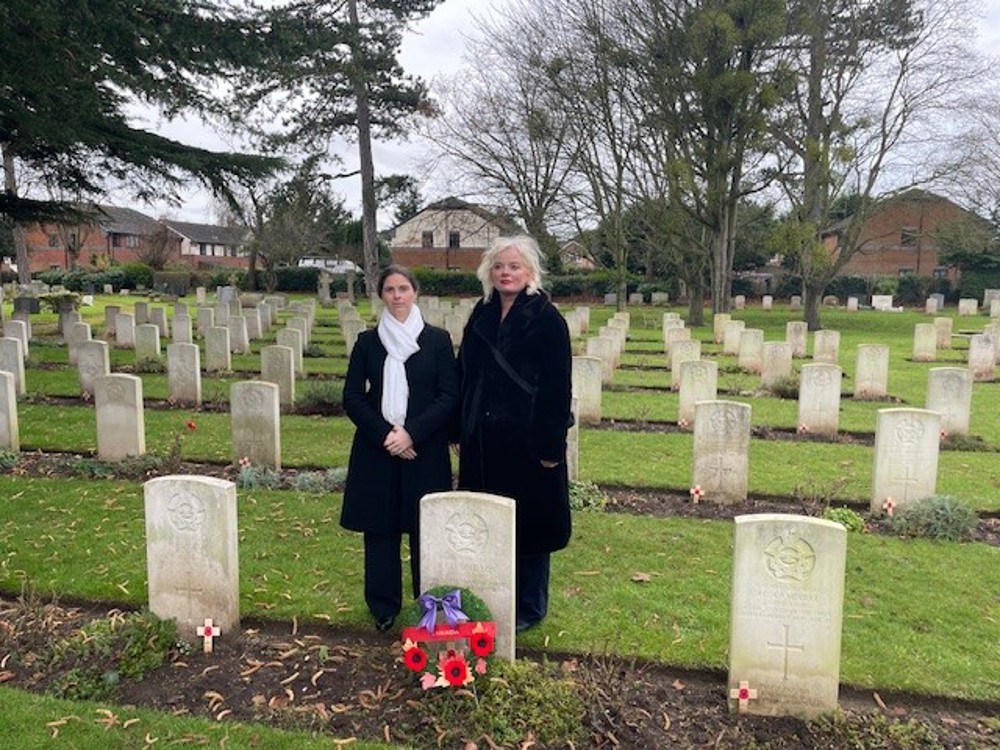 Two members of the Maple Leaf Trust pose behind a CWGC headstone in Stratford-upon-Avon Cemetery. A wreath has been laid on the CWGC headstone.