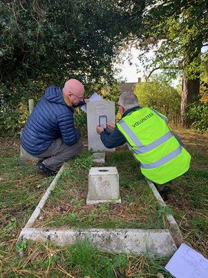 Two middle aged men inspecting a CWGC headstone with a smartphone.