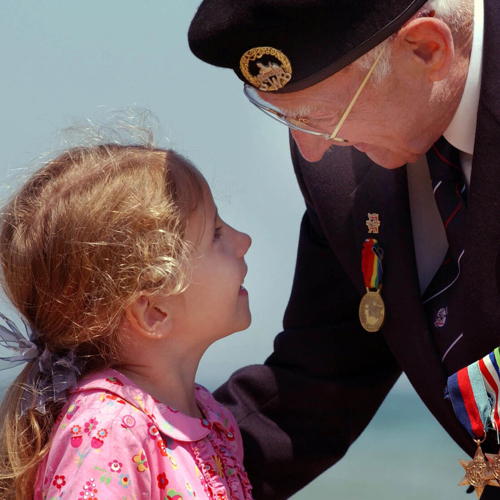 A Normandy Veteran speaking to a little girl in a pink dress.