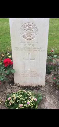 The white Portland stone headstone of Private Graham Nye. The capbadge of the Hampshire Regiment, showing a tiger astride a rose framed by a laurel wreath, is clearly visible.