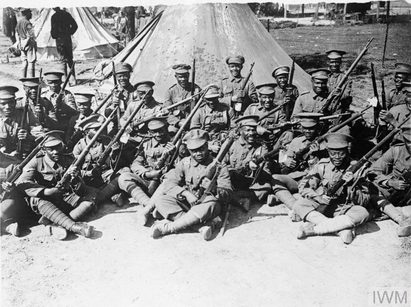 Black British West Indies Regiment soldiers posing with their rifles in front of their tents, 1916.