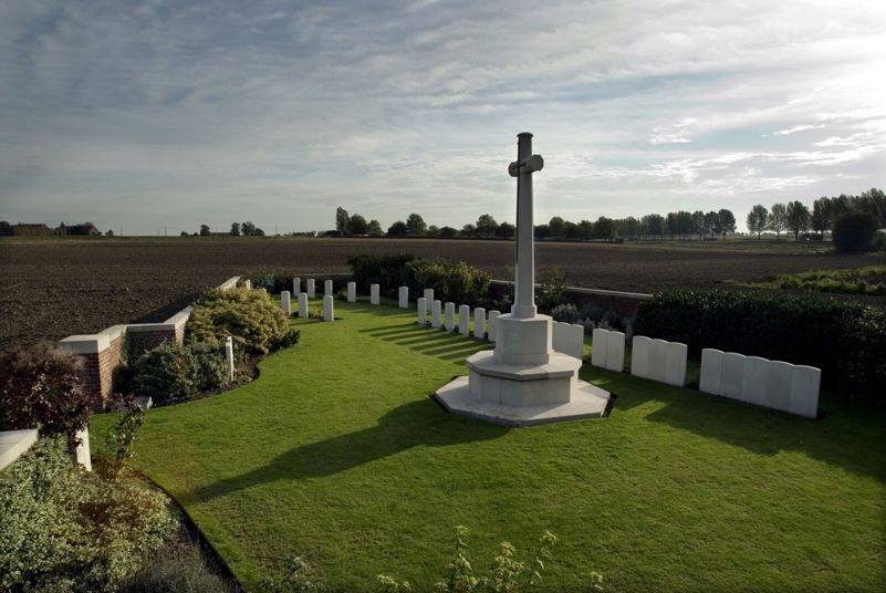 La Belle Alliance Cemetery with Cross of Sacrifice prominent in the foreground. A row of headstones runs behind the cross. A circle of war graves can also be seen toward the rear end of the cemetery,