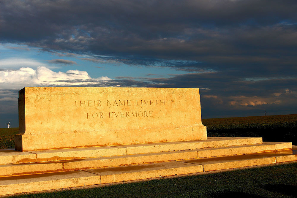 A CWGC Stone of Remembrance silhouetted against a stormy sky.