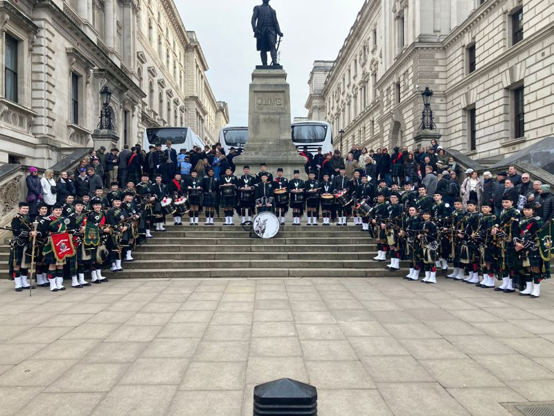 The pipe and drum band in their tartan uniforms pose next to the Clive of India memorial in London.