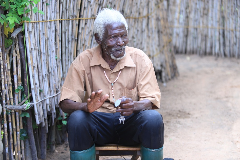 An old Tanzanian man sitting on a stool telling a story.