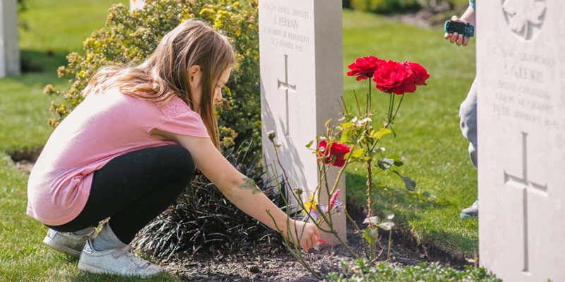 A girl in a pink shirt lays flowers on a CWGC headstone.