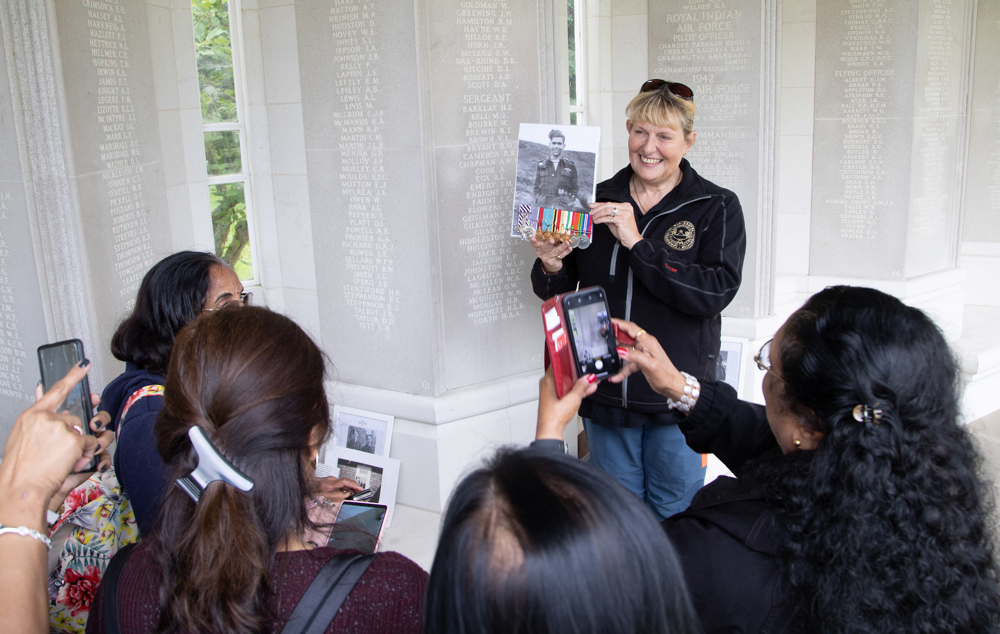A tour guide holds up a picture of a WW2 veteran and his medals to a group of interest tourgoers at the Runnymede Memorial.
