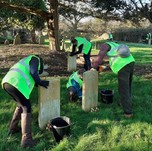 Men in high vis vests scrubbing war grave headstones