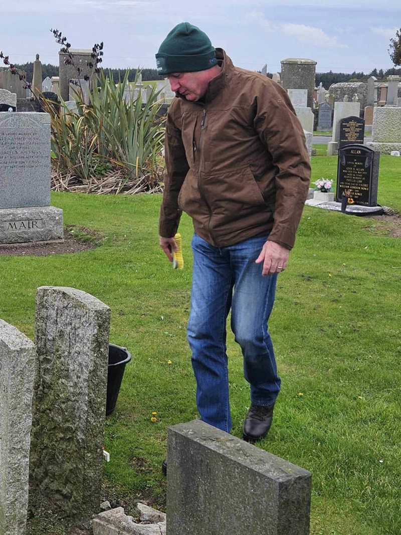 Man in beanie hate inspecting war graves in a Scottish cemetery.