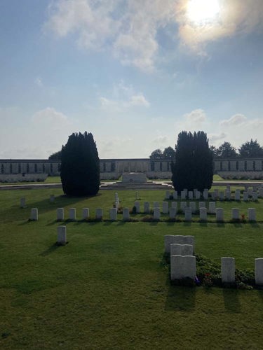 Stone of Remembrance at Tyne Cot Cemetery. The stone is flanked by two tall trees. War graves can be seen in the foreground.