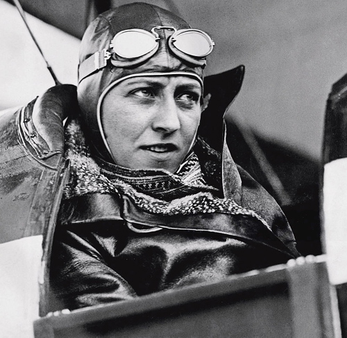 Portrait of Amy Johnson CBE in flying gear in the cockpit of a bi-plane.