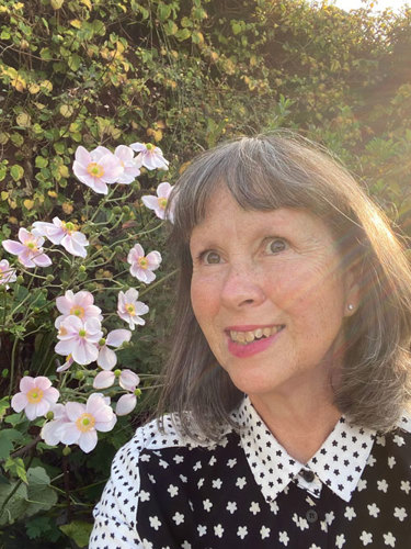 Portrait of Sarah Holmes in front of bushes and flowers in her garden.