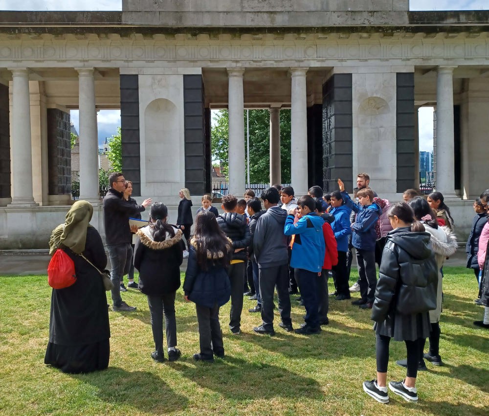 A pair of Commonwealth War Graves speakers holding a talk to a group of schoolchildren in front of the Tower Hill Memorial.