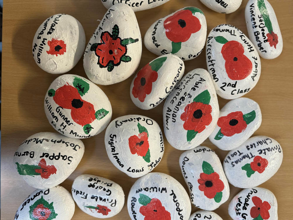 Stones painted white and decorated with hand painted poppies and casualty names.