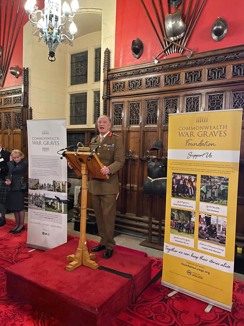 Major General Alastair Bruce delivering a speech on a lectern at Edinburgh Castle. He is standing in front of two roller banners with Commonwealth War Graves branding .