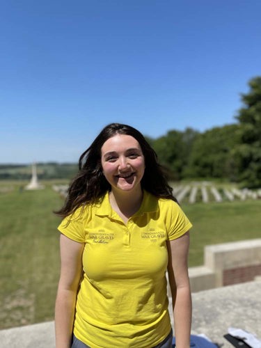 Annabel poses in a yellow CWGF polo shirt in front of the graves at the Thiepval Memorial