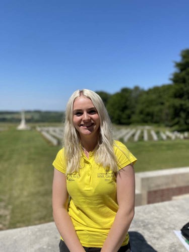 Eleanor poses in a yellow CWGF polo shirt in front of the graves at the Thiepval Memorial