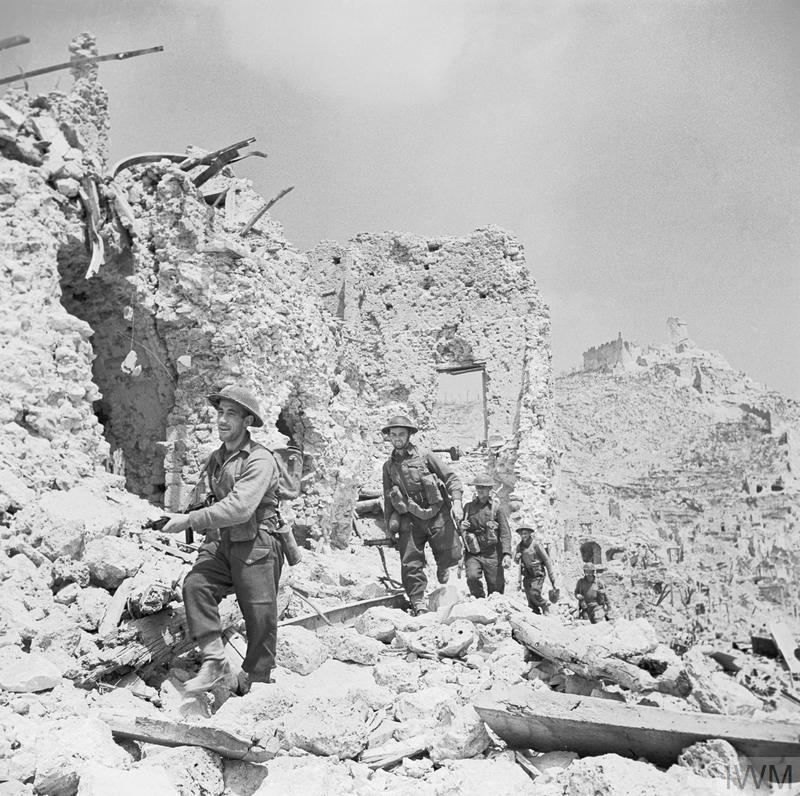 Soldiers advance through the rubble and wrecked buildings of Monte Cassino during the WW2 Italian Campaign