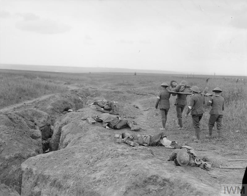 WW1 era british soldiers carry a wounded soldier on a stretcher past the corpses of several fallen comrades.