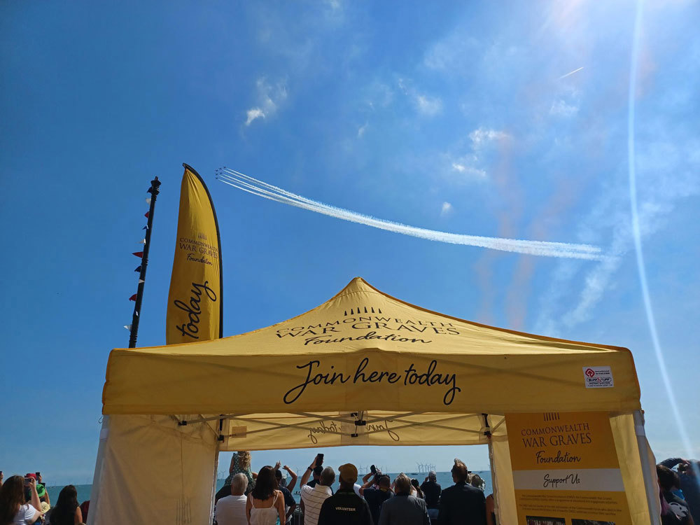 Red Arrows pass through the sky above a Commonwealth War Graves Foundation tent.