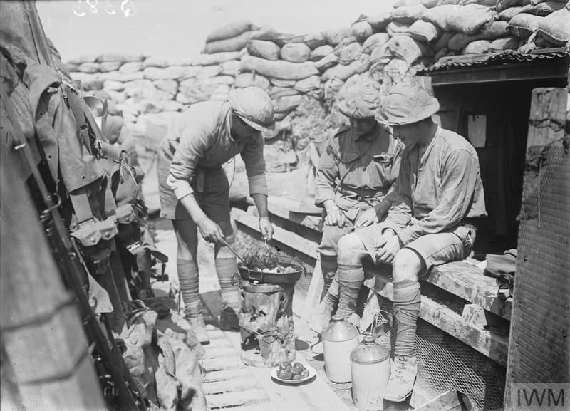 Australian First World War soldiers cooking a meal on a frying pan over a fire in their trench dugout on the Western Front circa 1916.