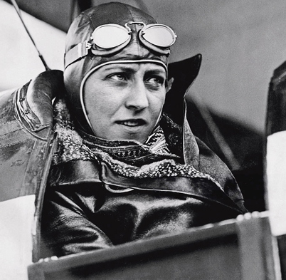 Black and white portrait of Amy Johnson wearing 1930s aviation goggles in the cockpit of an aircraft.